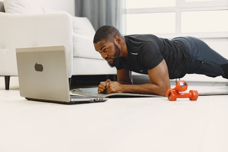 Adult man doing a plank exercise at home while following a workout on a laptop.